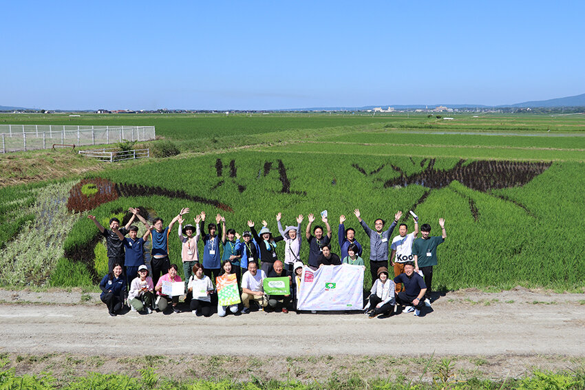 田んぼアートの前で集合写真をとる参加者