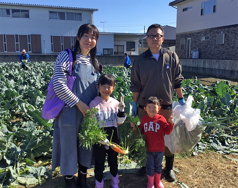 収穫した野菜を手にほほえむ参加者の写真